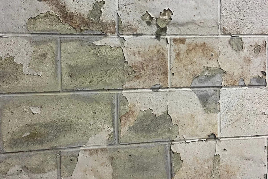 Close-up of peeling paint and exposed substrate on an interior CMU block wall in a warehouse 