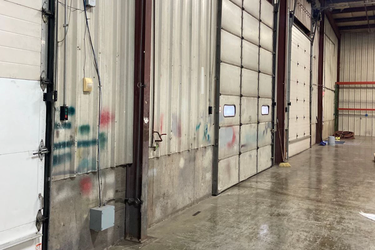 Warehouse interior wall near overhead doors with visible wear, staining, and scuffed surfaces before repainting 